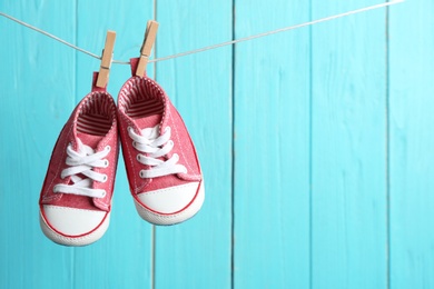 Photo of Baby shoes on laundry line against color wooden background, space for text. Child accessories