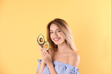 Portrait of young beautiful woman with ripe delicious avocado on color background