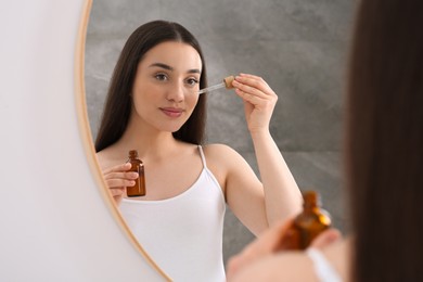 Woman applying essential oil onto face near mirror