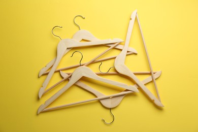 Wooden hangers on yellow background, top view