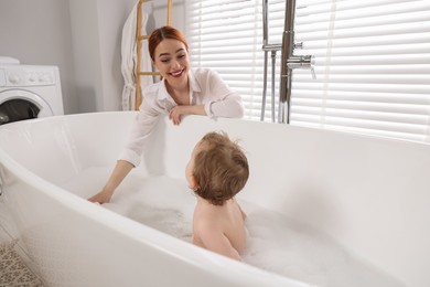 Mother washing her little baby in tub at home