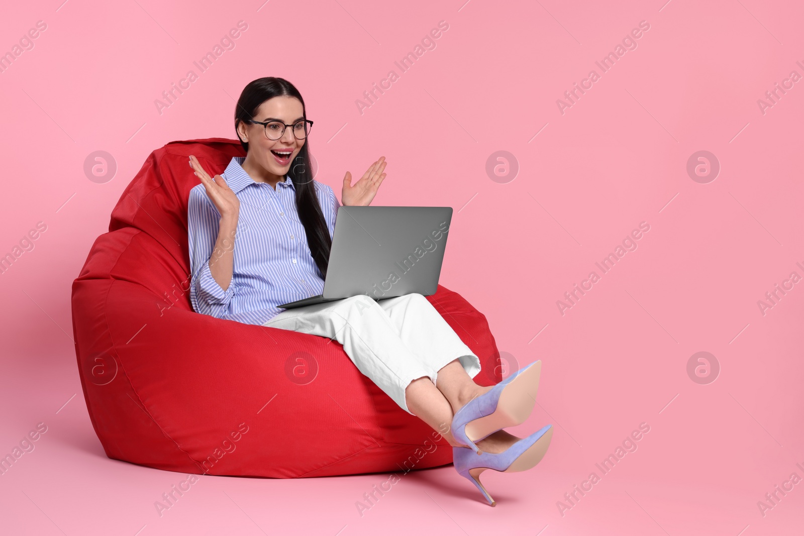 Photo of Surprised woman with laptop sitting on beanbag chair against pink background