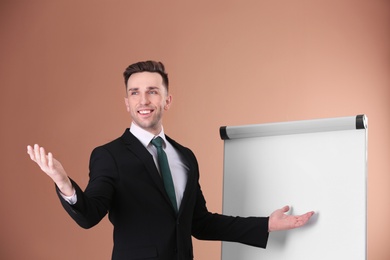 Young business trainer near flip chart on color background