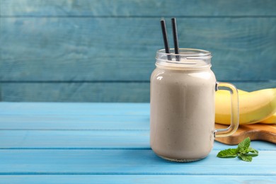 Mason jar with banana smoothie on light blue wooden table. Space for text
