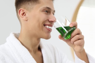 Photo of Young man using mouthwash indoors, closeup view