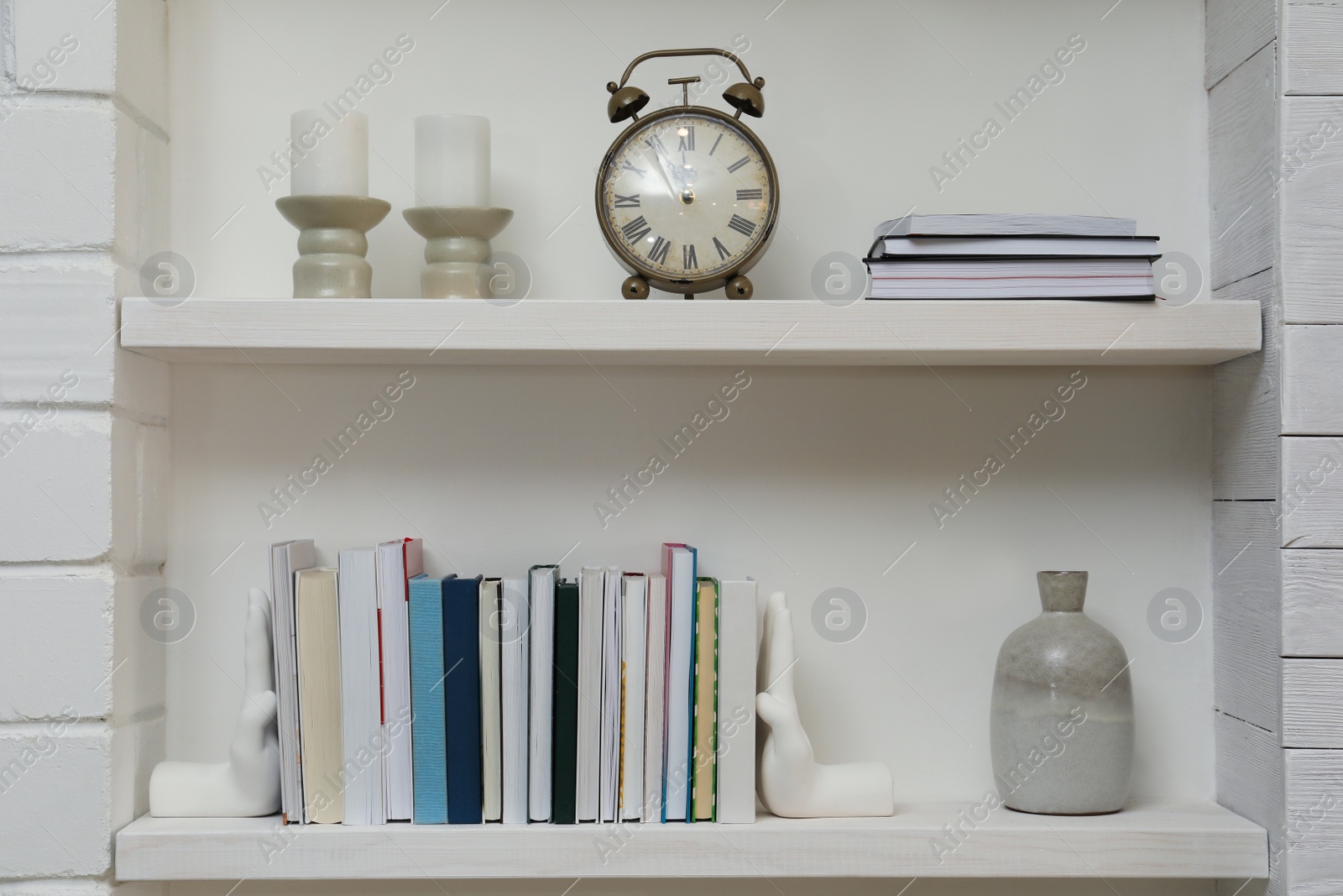 Photo of Hand shaped bookends with books and decor on shelves indoors. Interior design