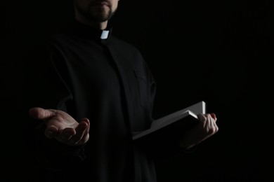Photo of Priest with Bible praying on dark background, closeup