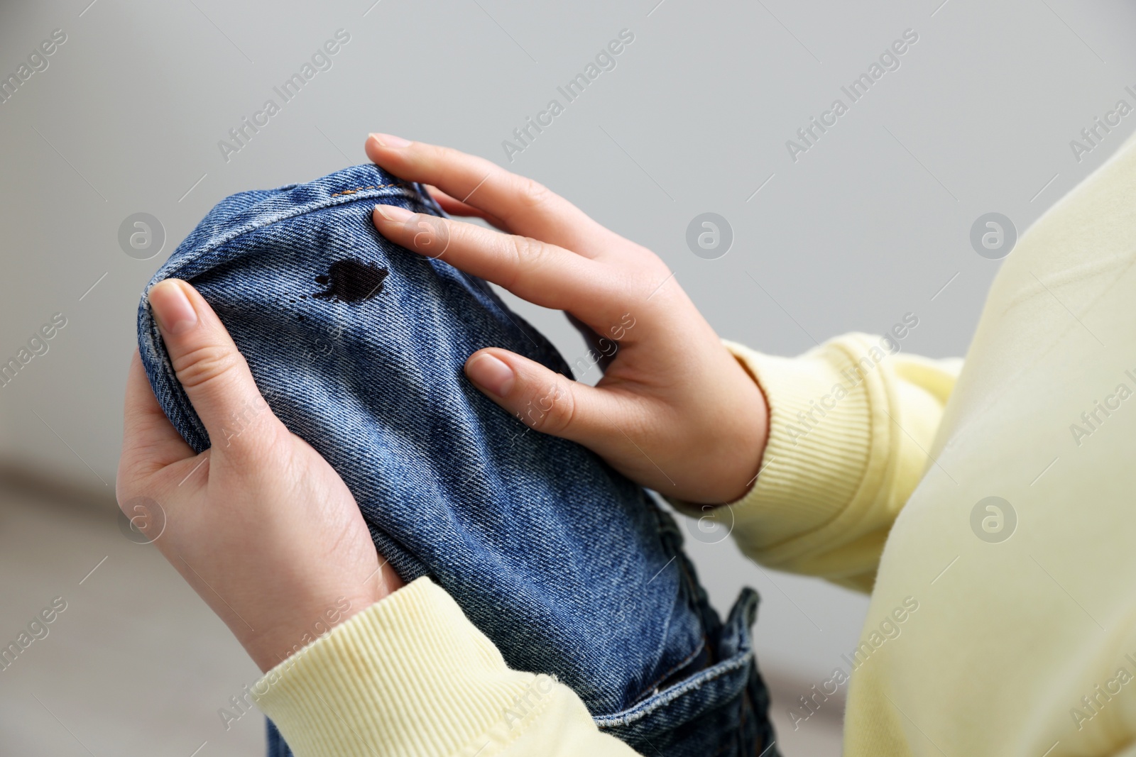 Photo of Woman holding jeans with black ink stain on blurred background, closeup