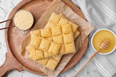 Wooden tray with delicious sweet kozinaki bars, sesame seeds and honey on white textured table, flat lay