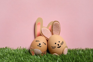 Photo of Easter eggs as cute bunnies on green grass against pink background