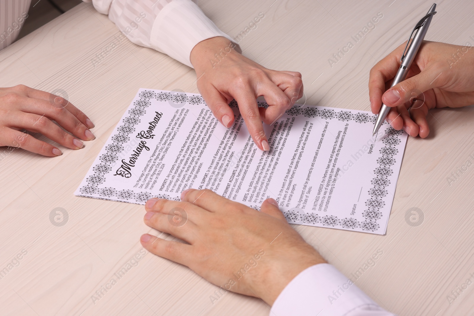 Photo of Man and woman signing marriage contract at light wooden table, closeup