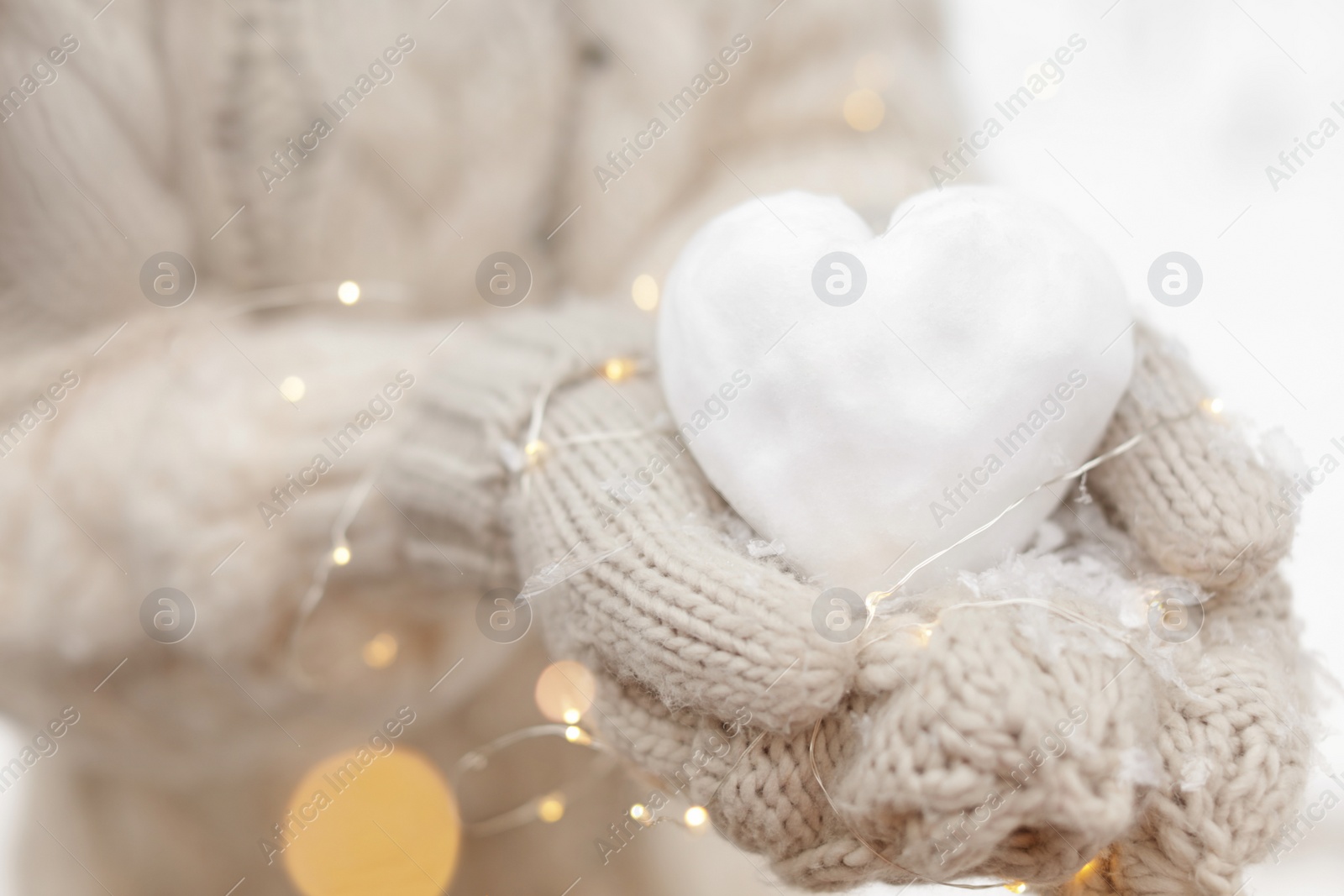 Photo of Woman holding Christmas lights and heart made of snow, closeup