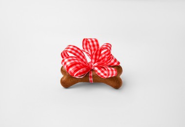 Photo of Bone shaped dog cookie with red bow on white background