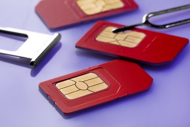 Photo of SIM cards, tray and ejector on violet background, closeup