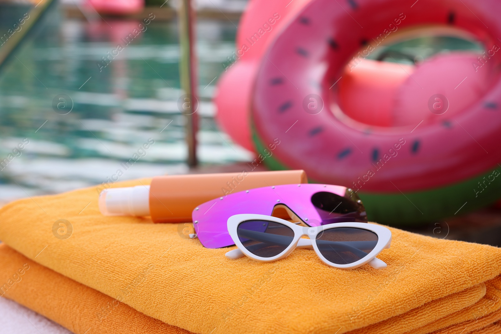 Photo of Beach towels, sunglasses and sunscreen on sunbed near outdoor swimming pool, closeup. Luxury resort