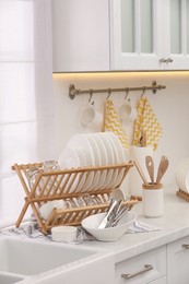 Drying rack with clean dishes and cutlery on countertop in kitchen