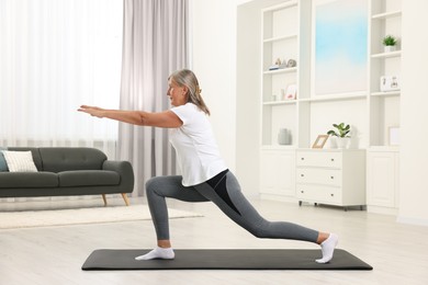 Photo of Senior woman practicing yoga on mat at home