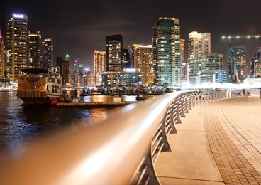 Photo of DUBAI, UNITED ARAB EMIRATES - NOVEMBER 03, 2018: Night cityscape with paved promenade and illuminated buildings near water canal