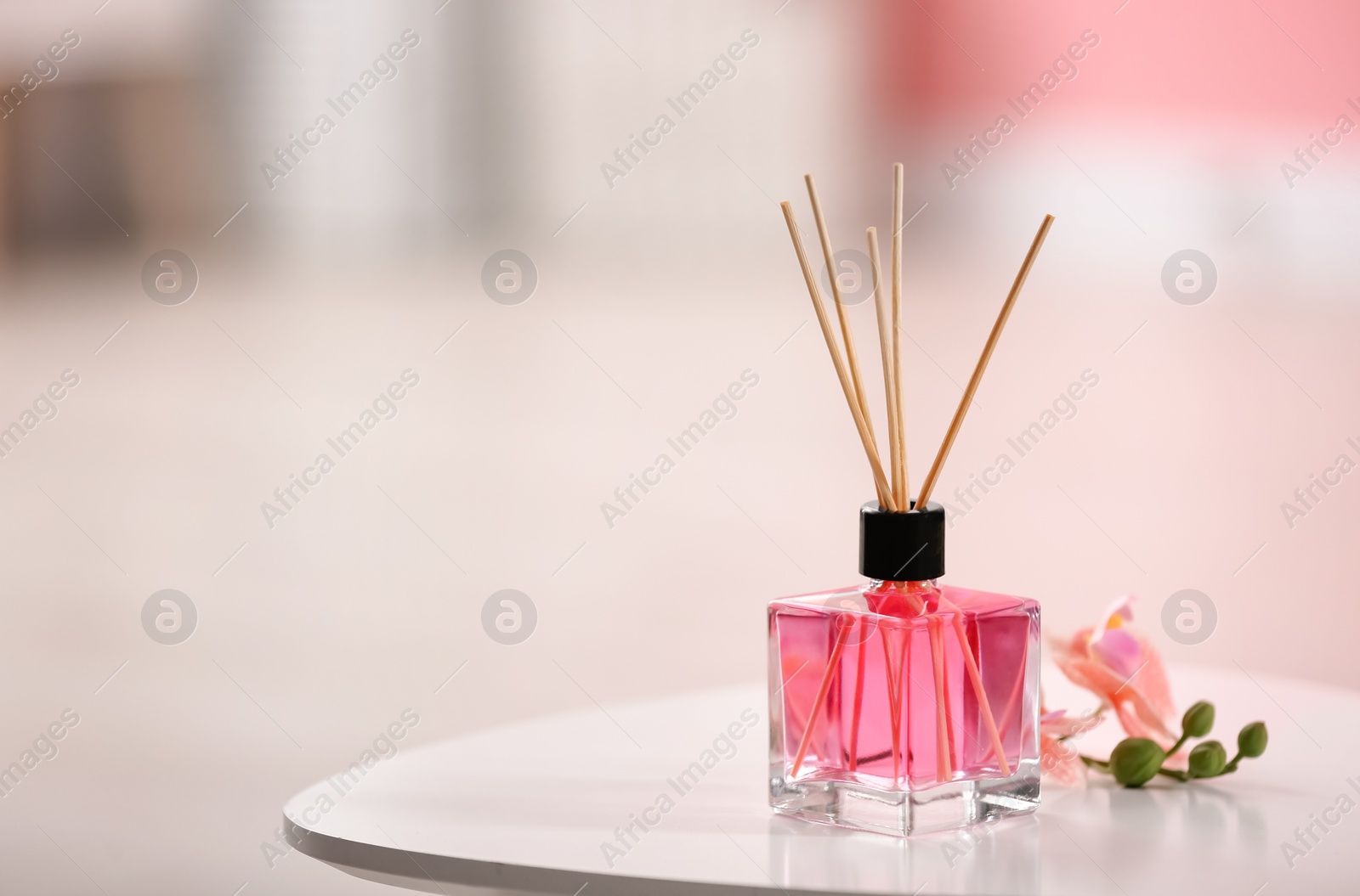 Photo of Aromatic reed air freshener and flowers on table against blurred background