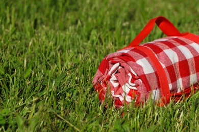 Photo of Rolled checkered picnic tablecloth on green grass, closeup. Space for text