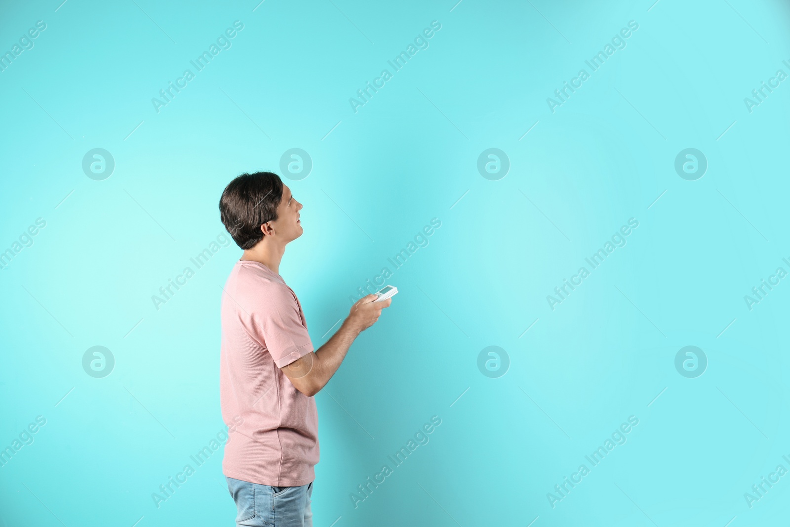 Photo of Young man with air conditioner remote on color background, copy space text