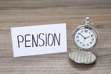 Photo of Card with word Pension and pocket watch on wooden table, closeup