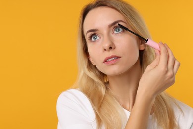 Beautiful woman applying mascara on orange background, space for text
