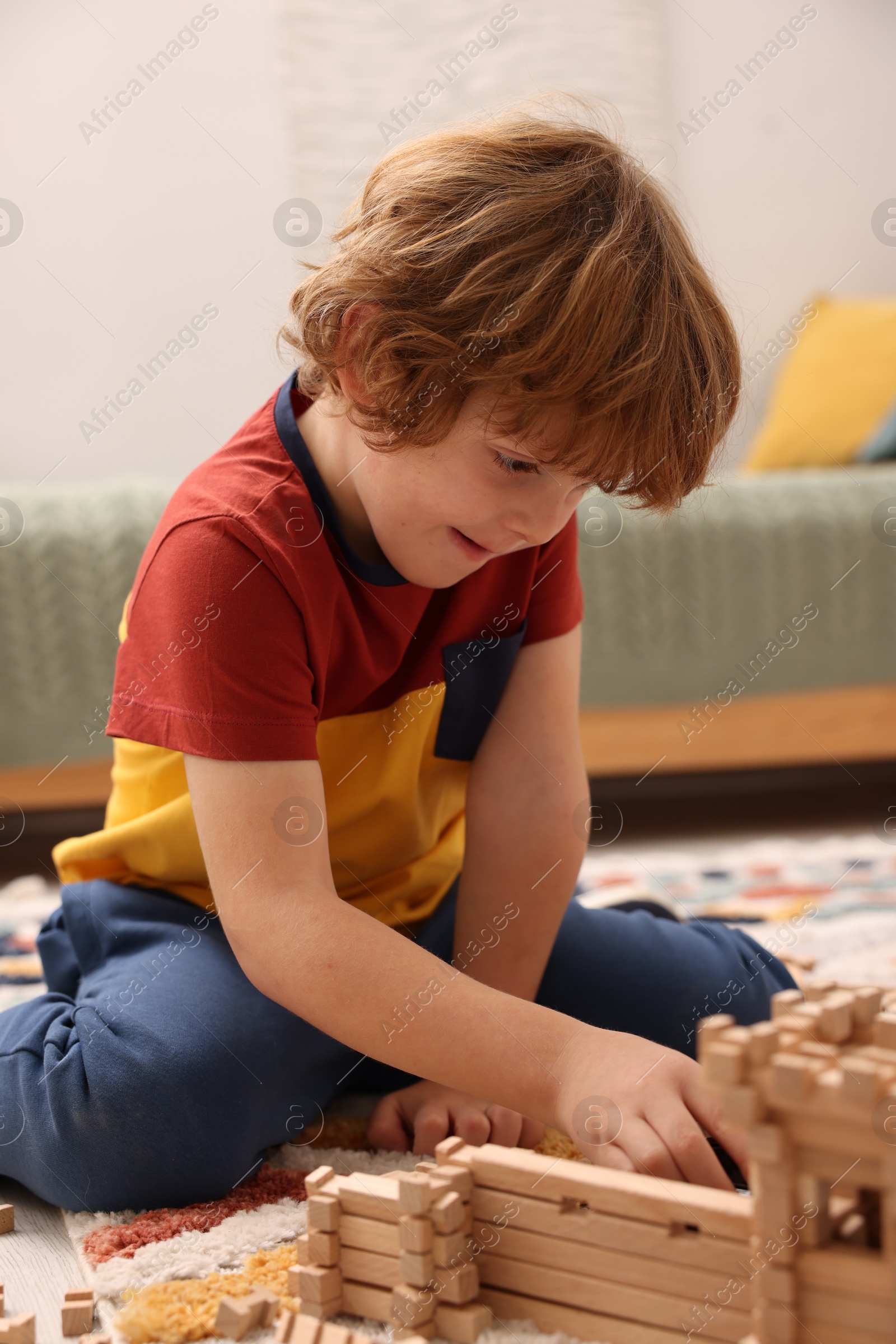 Photo of Little boy playing with wooden construction set on carpet in room. Child's toy