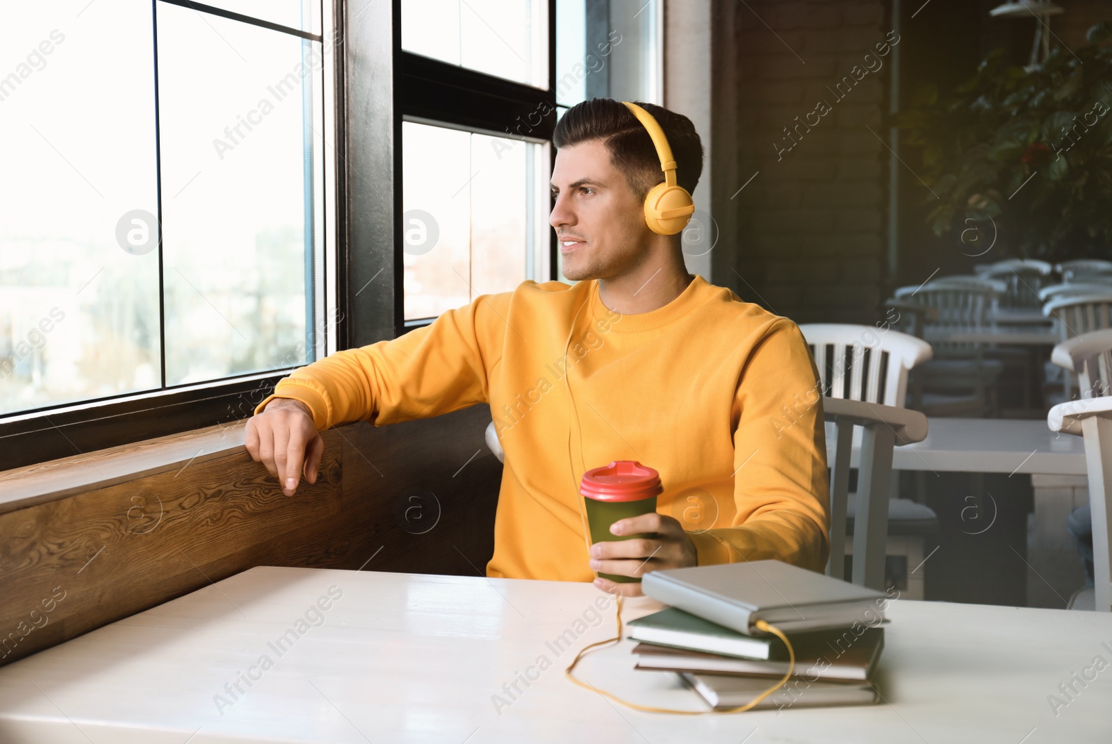 Photo of Man with headphones connected to book at table in cafe