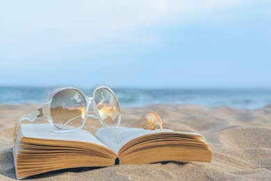 Beautiful sunglasses, book and shell on sand near sea, space for text