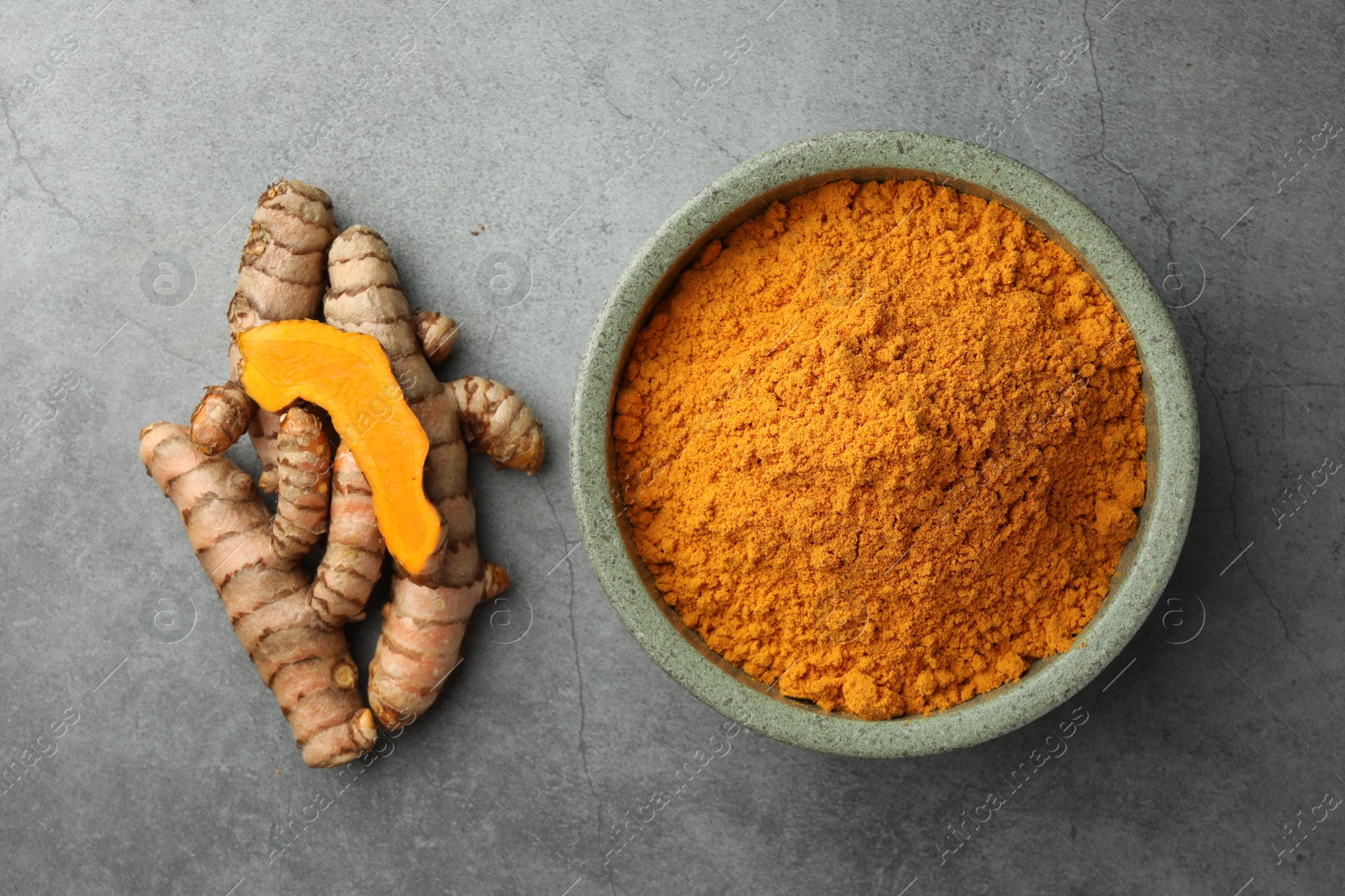 Photo of Bowl with turmeric powder and raw roots on grey table, flat lay
