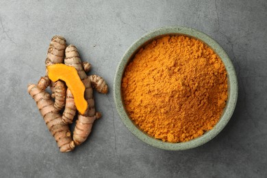 Bowl with turmeric powder and raw roots on grey table, flat lay