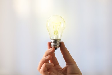 Photo of Woman holding light bulb on blurred background, closeup