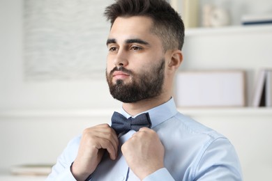 Portrait of handsome man adjusting bow tie indoors