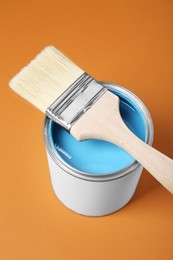 Can of light blue paint with brush on pale orange background, above view