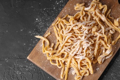 Photo of Board with homemade pasta and flour on dark textured table, top view. Space for text