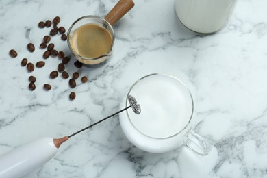 Photo of Mini mixer (milk frother), cup of milk and coffee on white marble table, flat lay