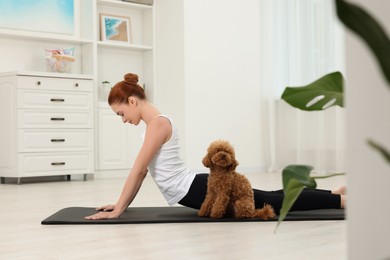 Photo of Young woman practicing yoga on mat with her cute dog at home