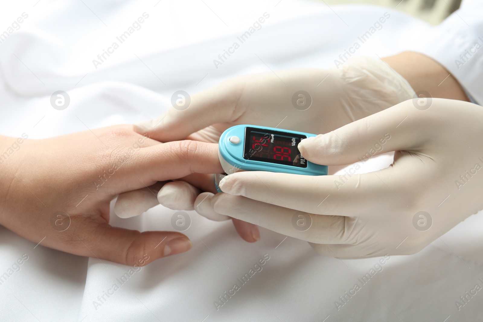 Photo of Doctor examining patient with fingertip pulse oximeter in bed, closeup