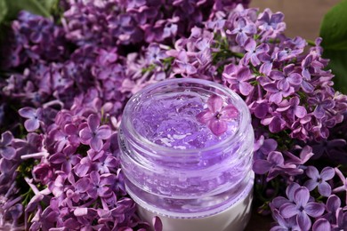 Photo of Jar of cosmetic product and lilac flowers on table