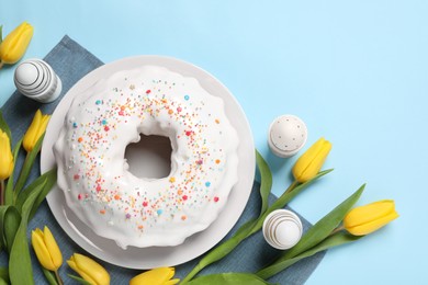 Photo of Delicious Easter cake decorated with sprinkles near beautiful tulips and painted eggs on light blue background, flat lay. Space for text