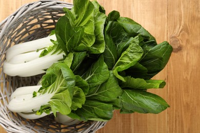 Fresh green pak choy cabbages in wicker basket on wooden table, top view