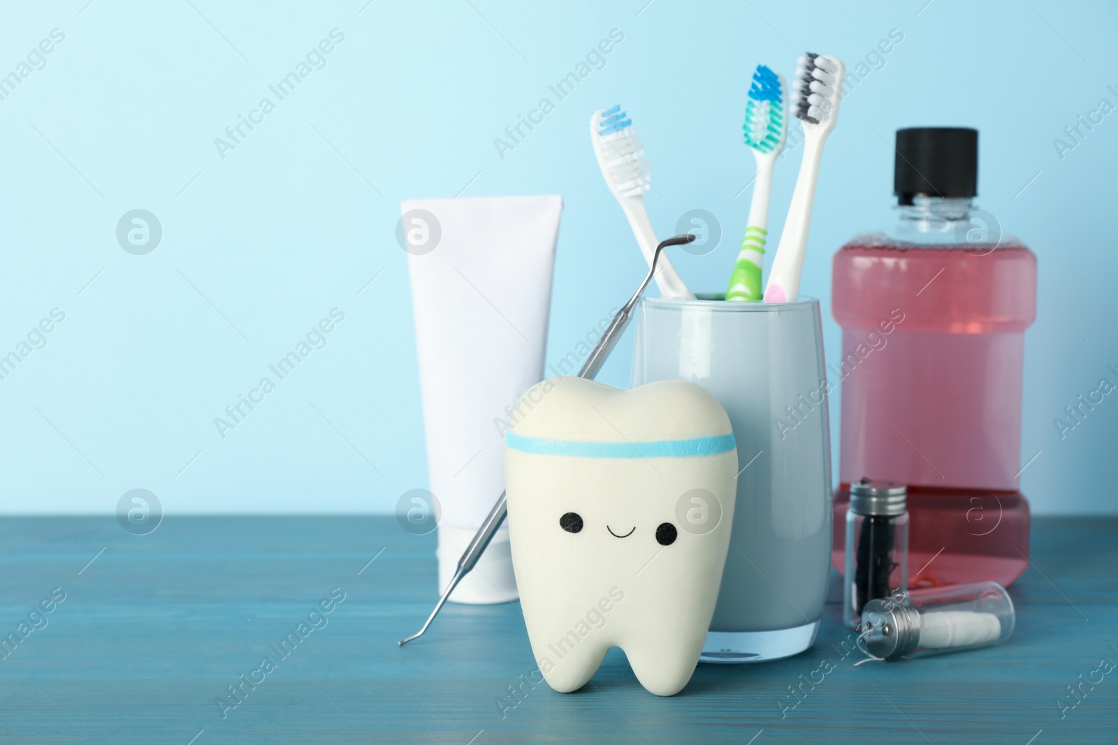 Photo of Tooth model, oral hygiene products and dentist tool on turquoise wooden table, space for text