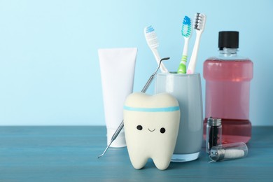 Photo of Tooth model, oral hygiene products and dentist tool on turquoise wooden table, space for text