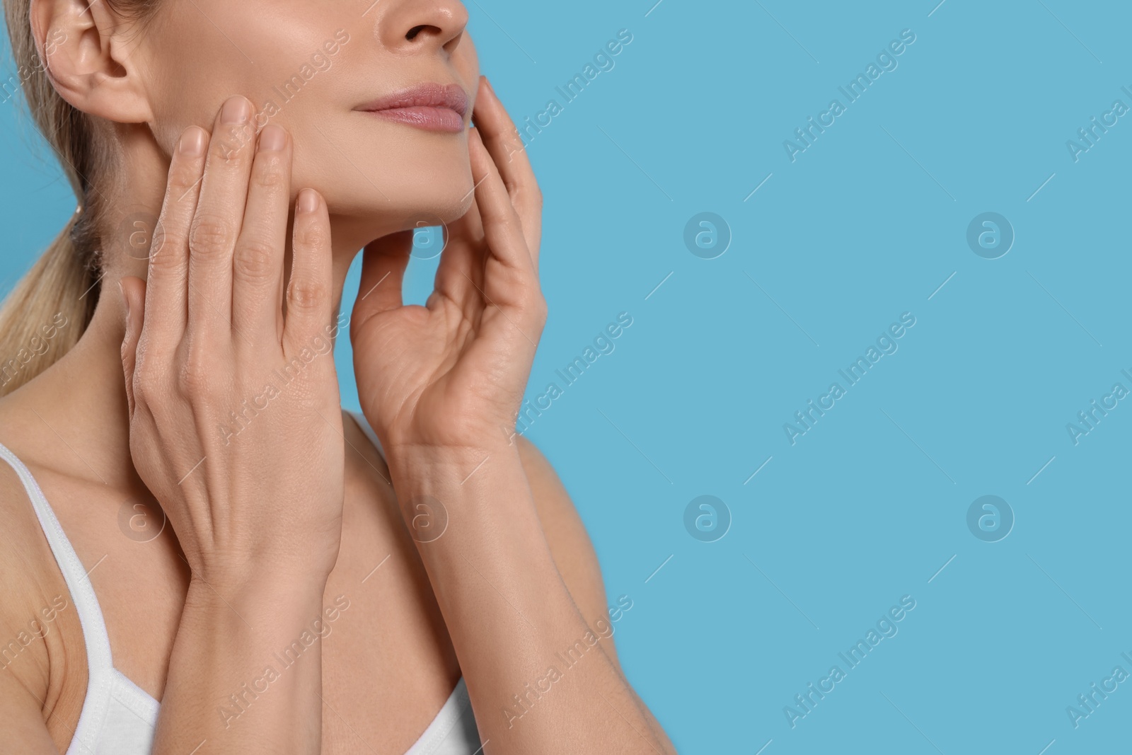 Photo of Woman massaging her face on turquoise background, closeup. Space for text
