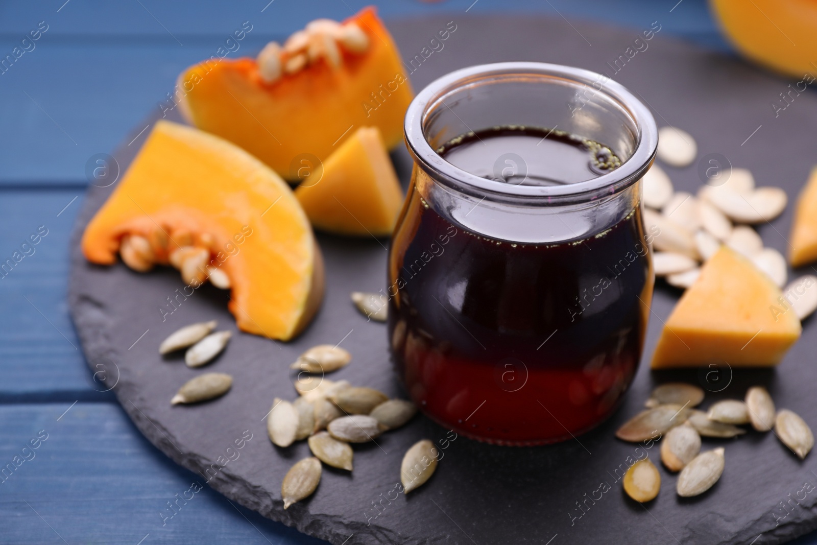 Photo of Fresh pumpkin seed oil in glass jar on blue wooden table