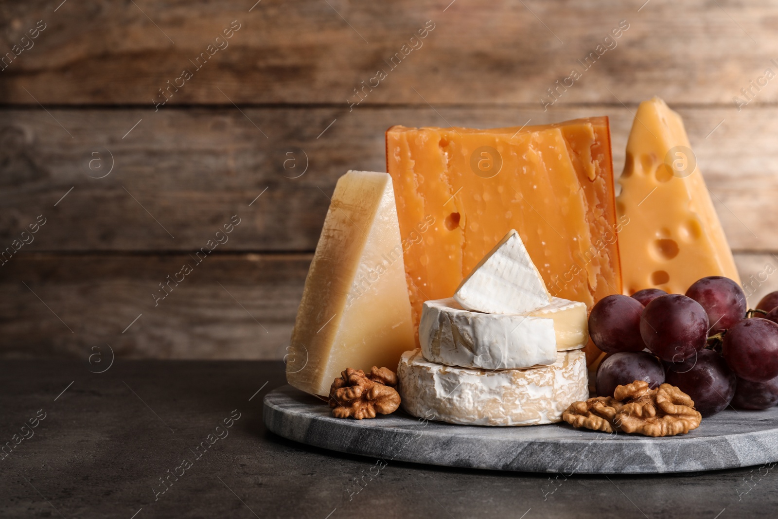 Photo of Composition with assorted cheese, grapes and walnuts on table against wooden background, space for text