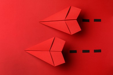 Photo of Handmade paper planes with dotted lines on red background, flat lay