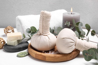 Photo of Spa composition with herbal massage bags and eucalyptus branches on white table