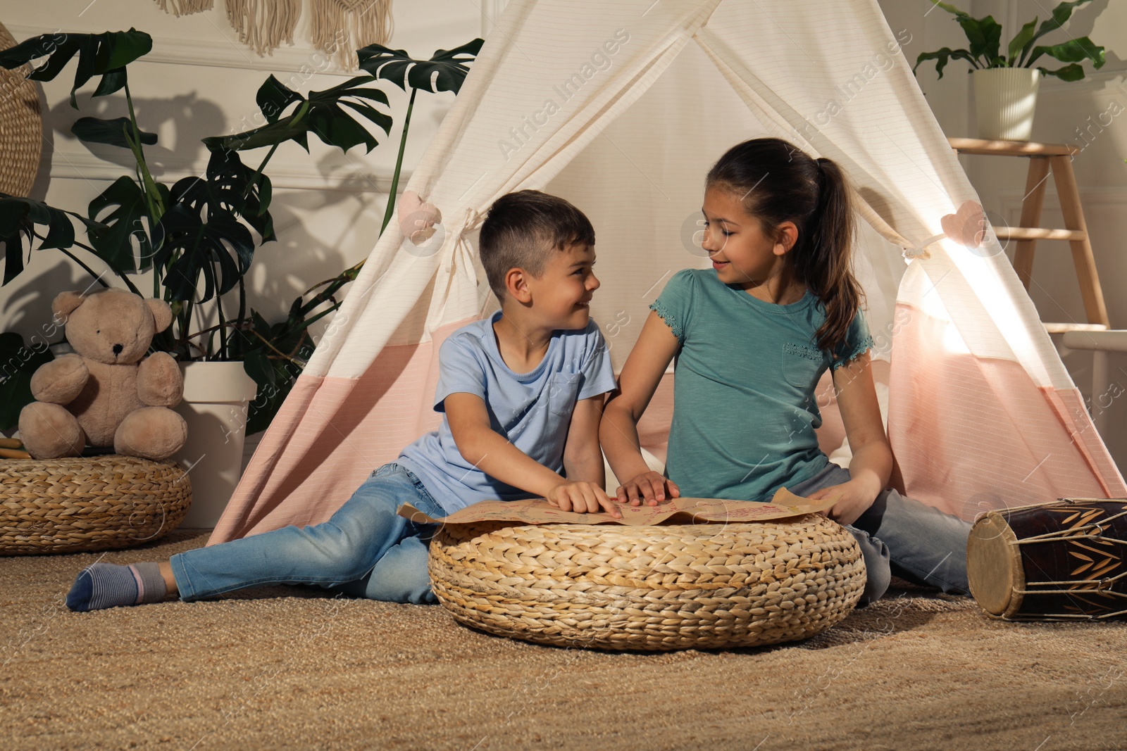 Photo of Cute little children with treasure map near toy wigwam at home